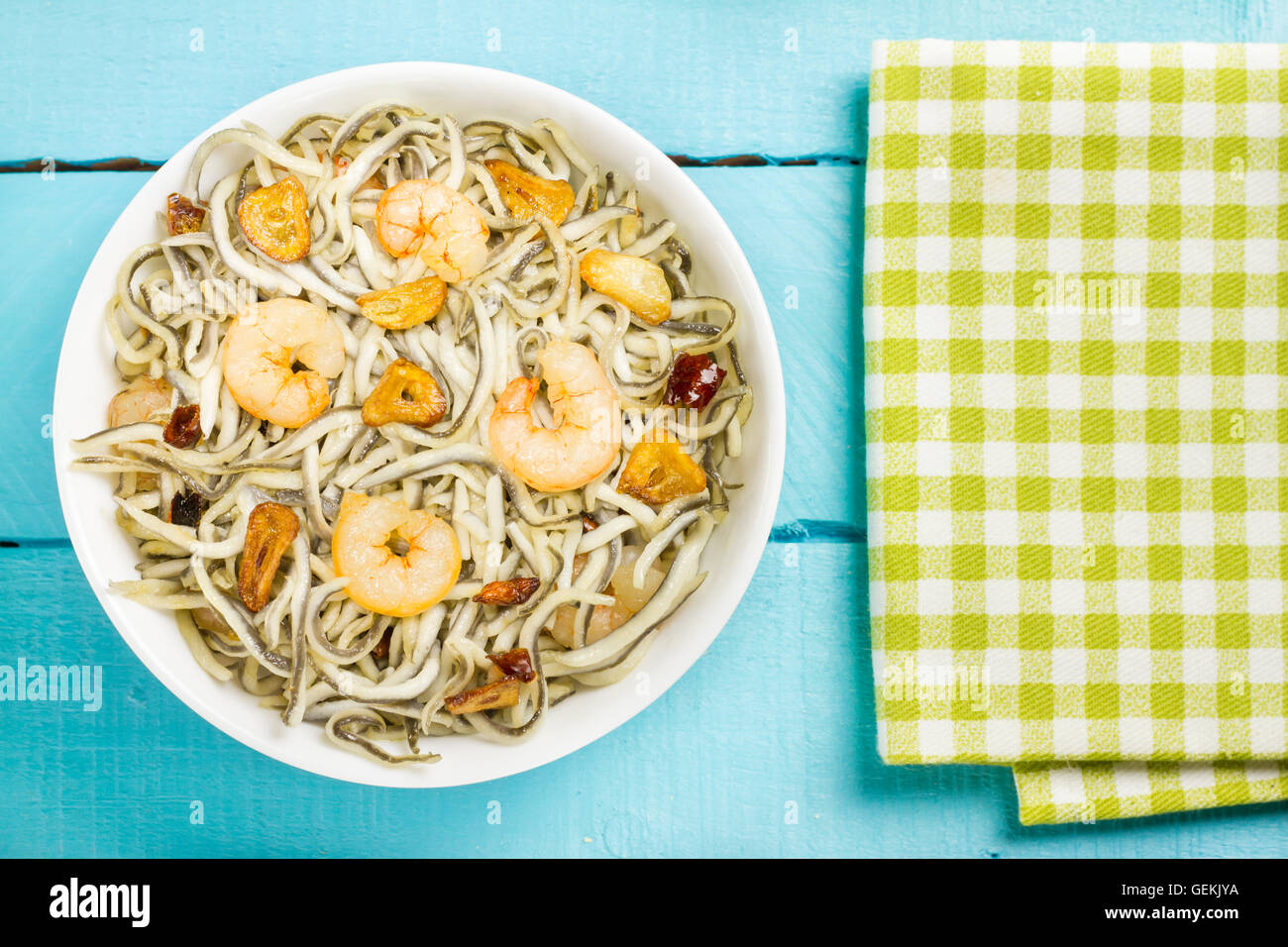 Surimi elvers with prawns, garlic and pepper on a white bowl and a green napkin on a blue wooden table Stock Photo