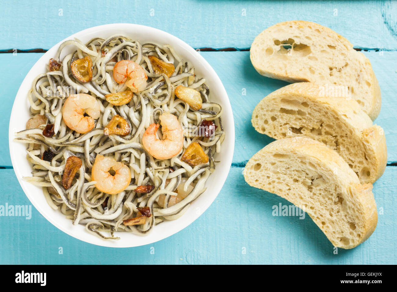 Surimi elvers with prawns, garlic and pepper on a white bowl, three slices of bread on a blue wooden table Stock Photo