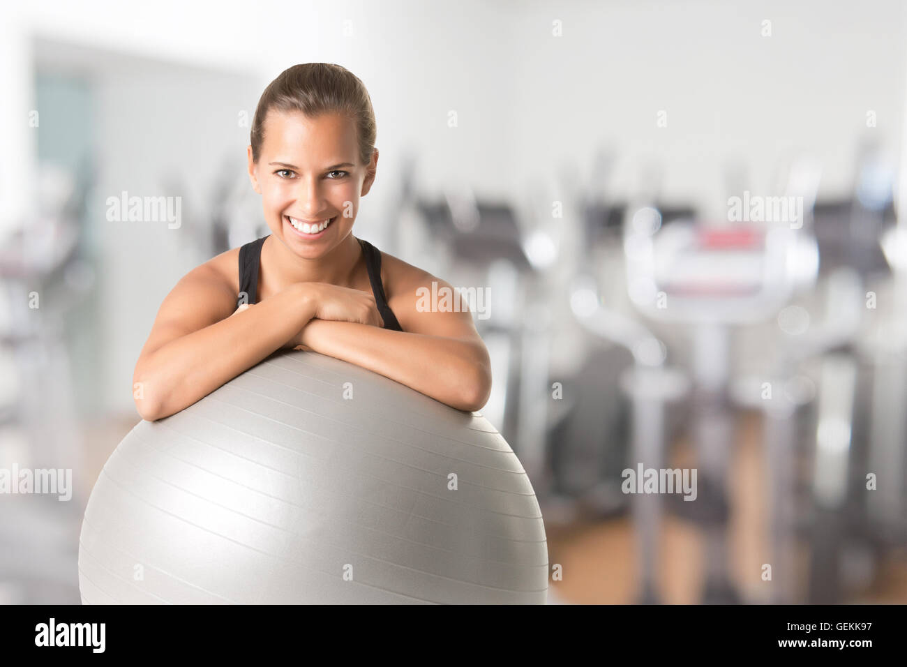 Fit woman sitting and holding a pilates ball on the floor, in a gym Stock Photo