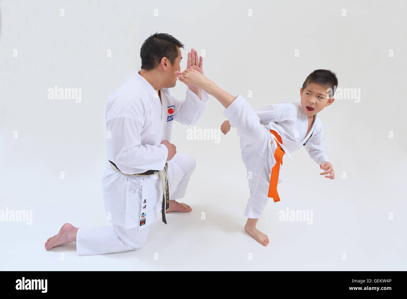 Japanese kid in karate uniform training with teacher on white
