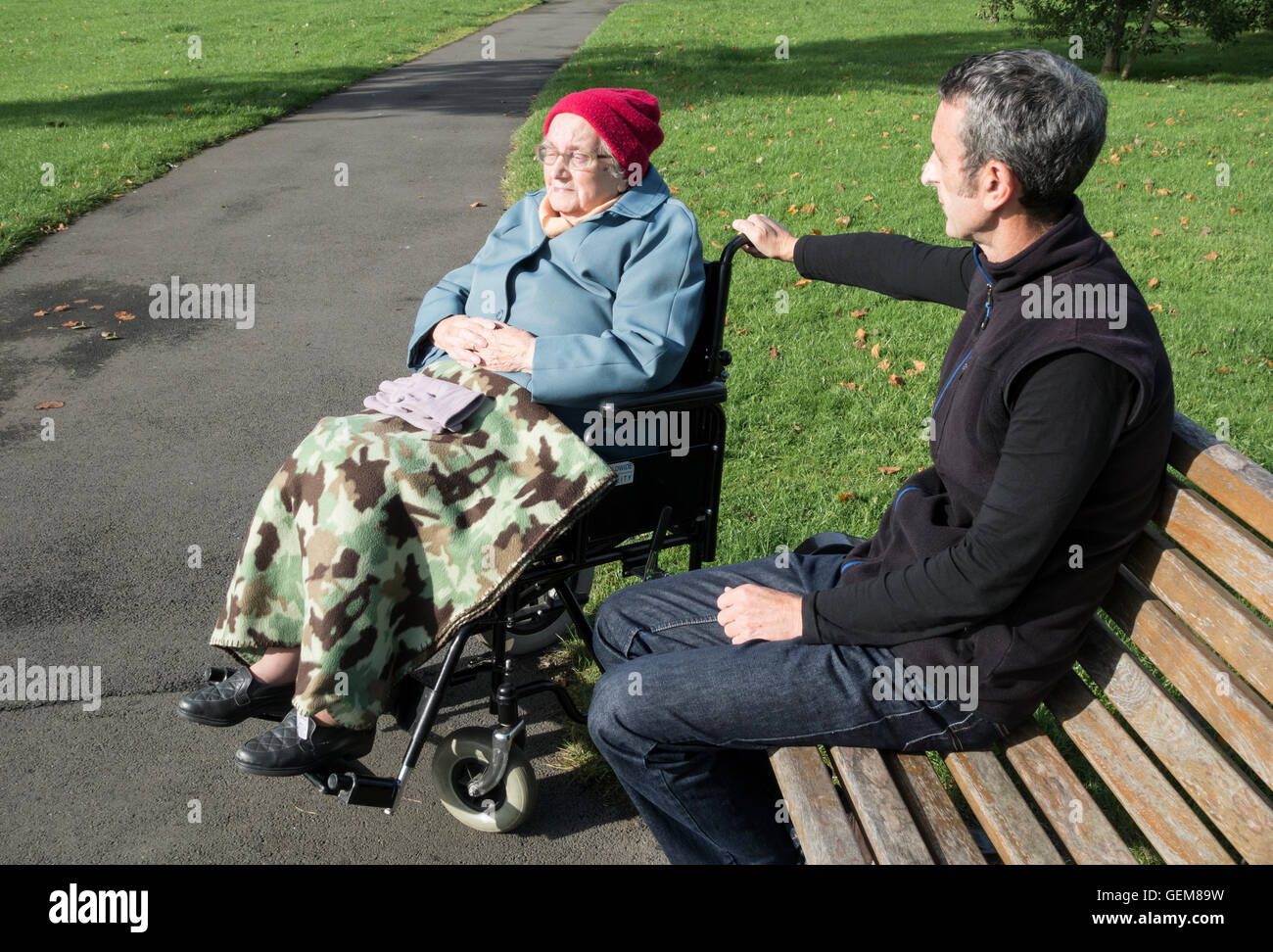 Carer (son) with 90 year old Mother in wheelchair in public park. UK Stock Photo