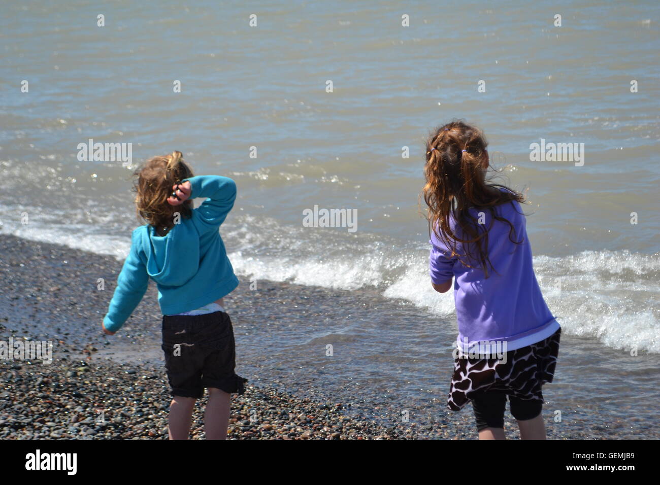 two girls throwing rocks into the lake from the shore. Stock Photo