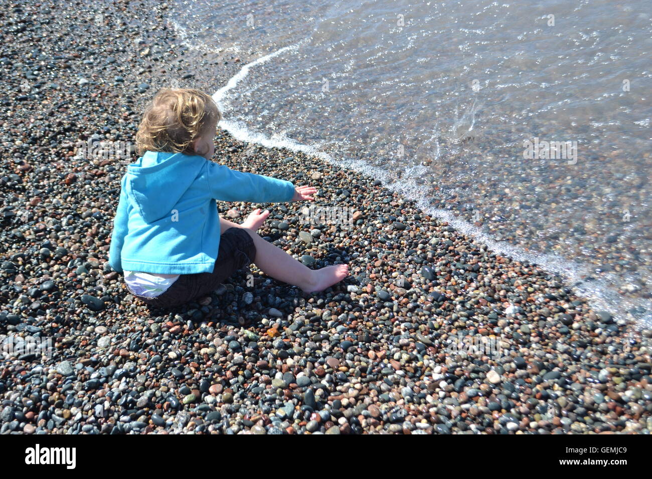 little girl playing on a cold day on a rocky beach.  with the desire to get her feet wet in the waves of lake superior. Stock Photo