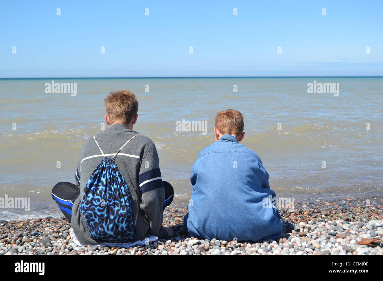 Two boys sitting on the rocky shore of lake superior Stock Photo