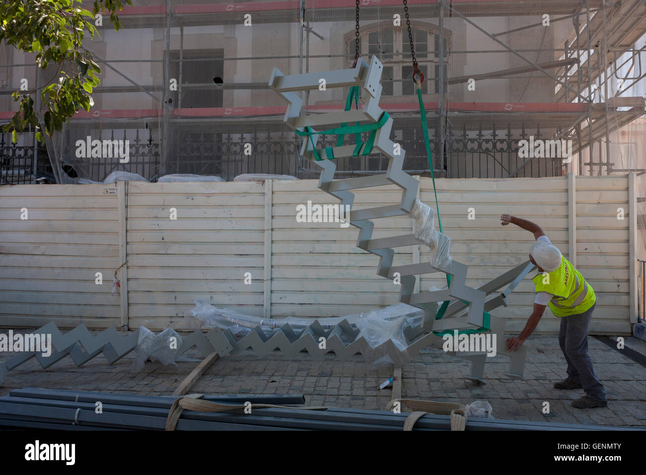 A construction worker signals to a crane operator to hoist some metal