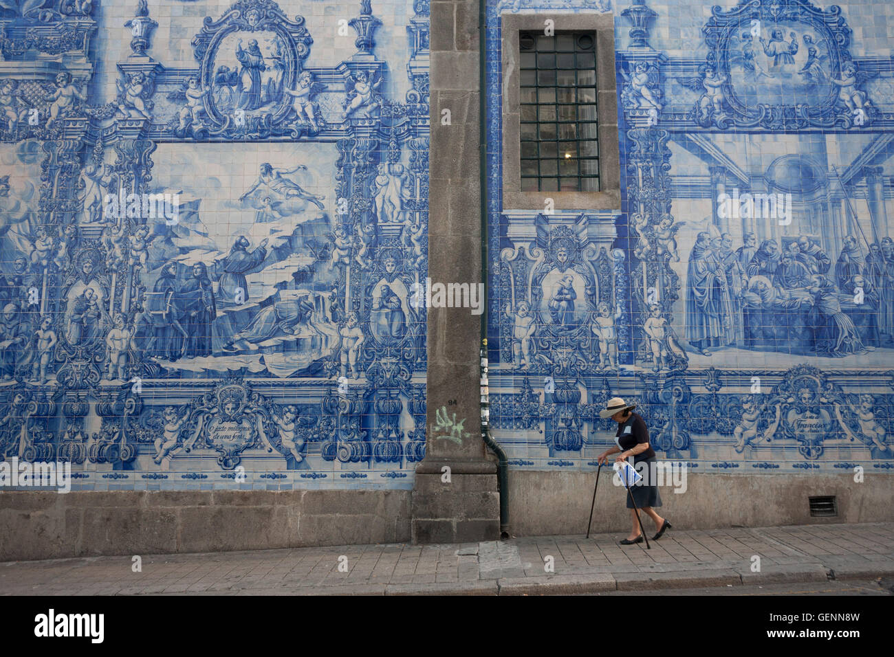A lady struggles with sticks beneath traditional Azulejo tiles on the wall of Capela Das Almas (church), on Rua Santa Catarina Stock Photo