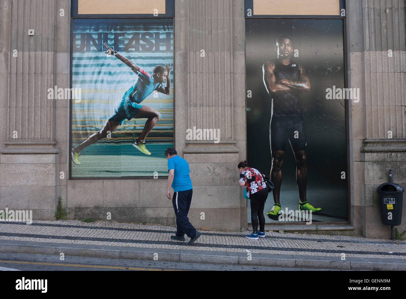 Two locals cough together beneath ad posters for sportswear outside a  sports shop in Porto, Portugal Stock Photo - Alamy