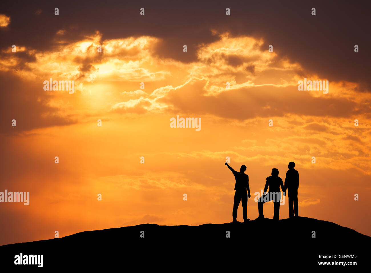 Landscape with silhouette of a standing man pointing finger in colorful sky and his friends on the high mountain peak against th Stock Photo