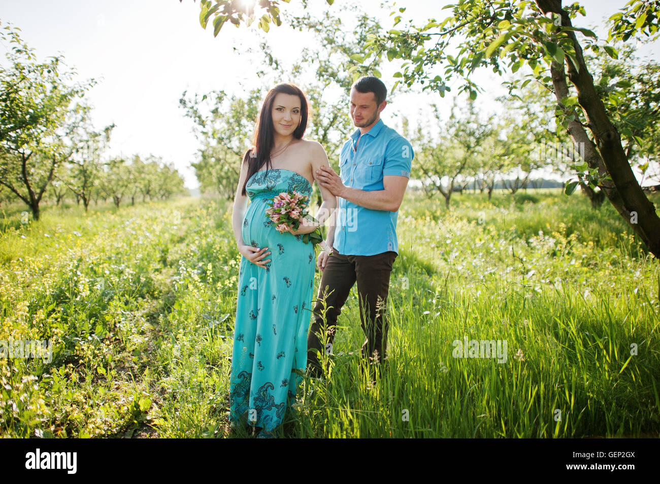Happy pregnant couple at turquoise dress on the garden Stock Photo - Alamy