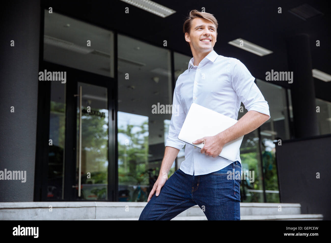 Cheerful successful young businessman with laptop walking to the office Stock Photo