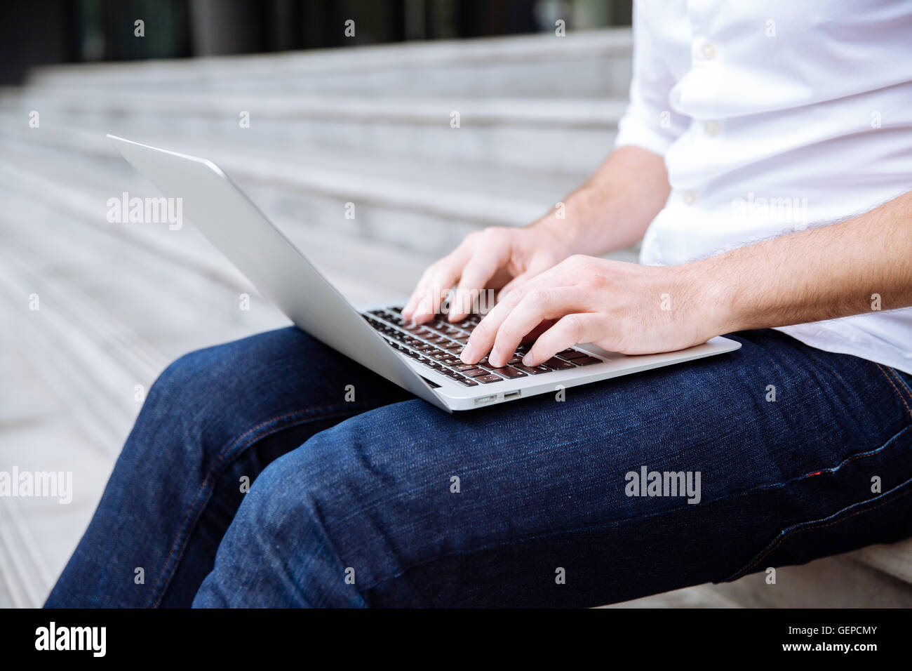 Closeup of young man sitting on stairs and using laptop Stock Photo - Alamy