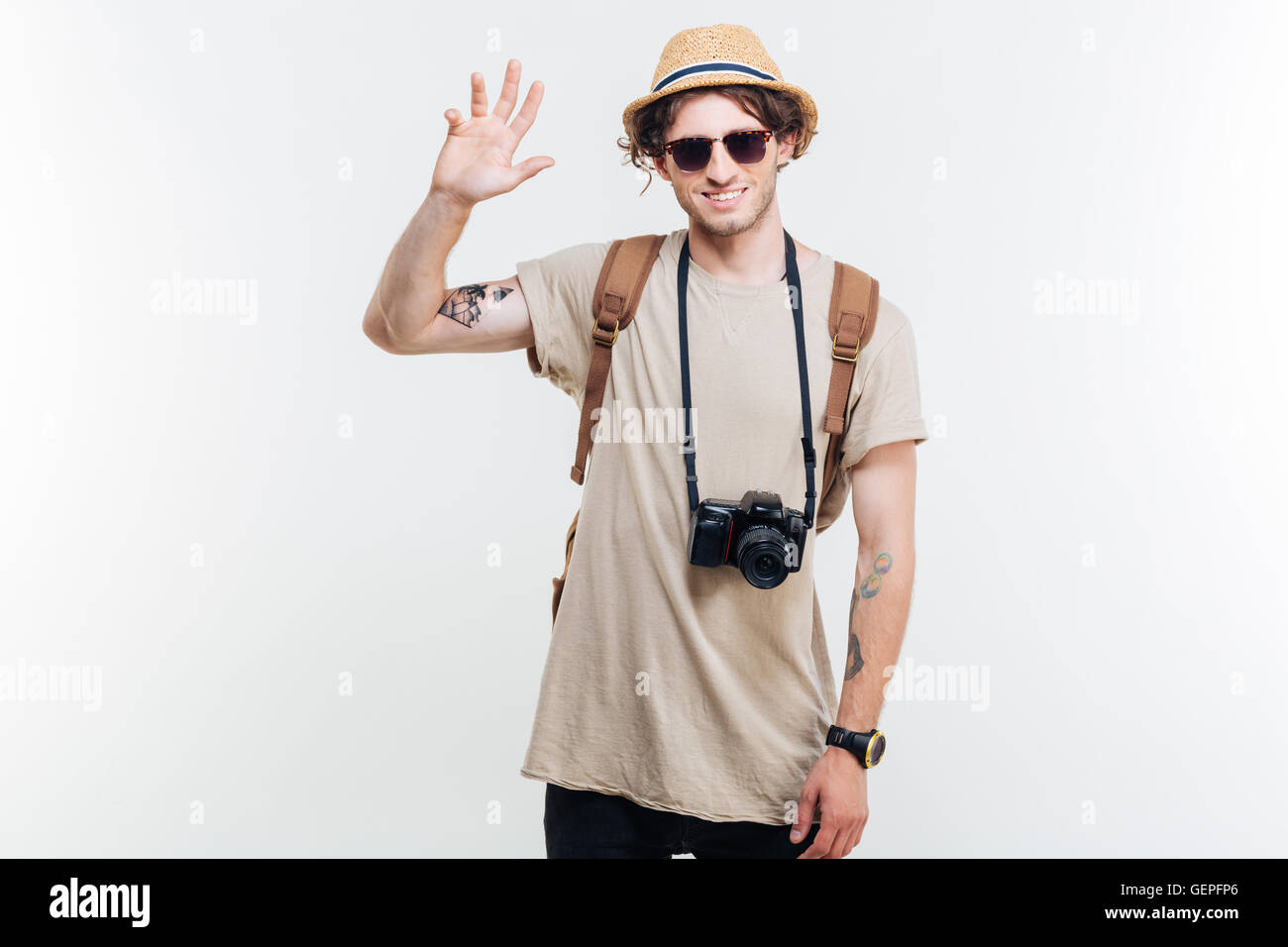 Portrait of a smiling young man with hat and backpack waving his hand ...