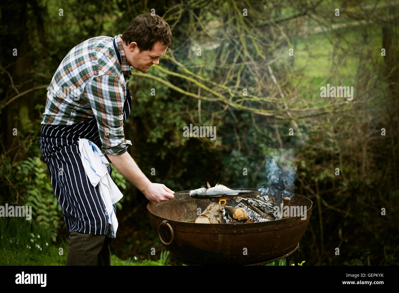 Chef standing in a garden, grilling a fish on a barbecue. Stock Photo