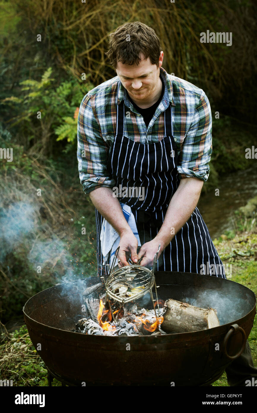 Chef standing in a garden, grilling a fish on a barbecue. Stock Photo