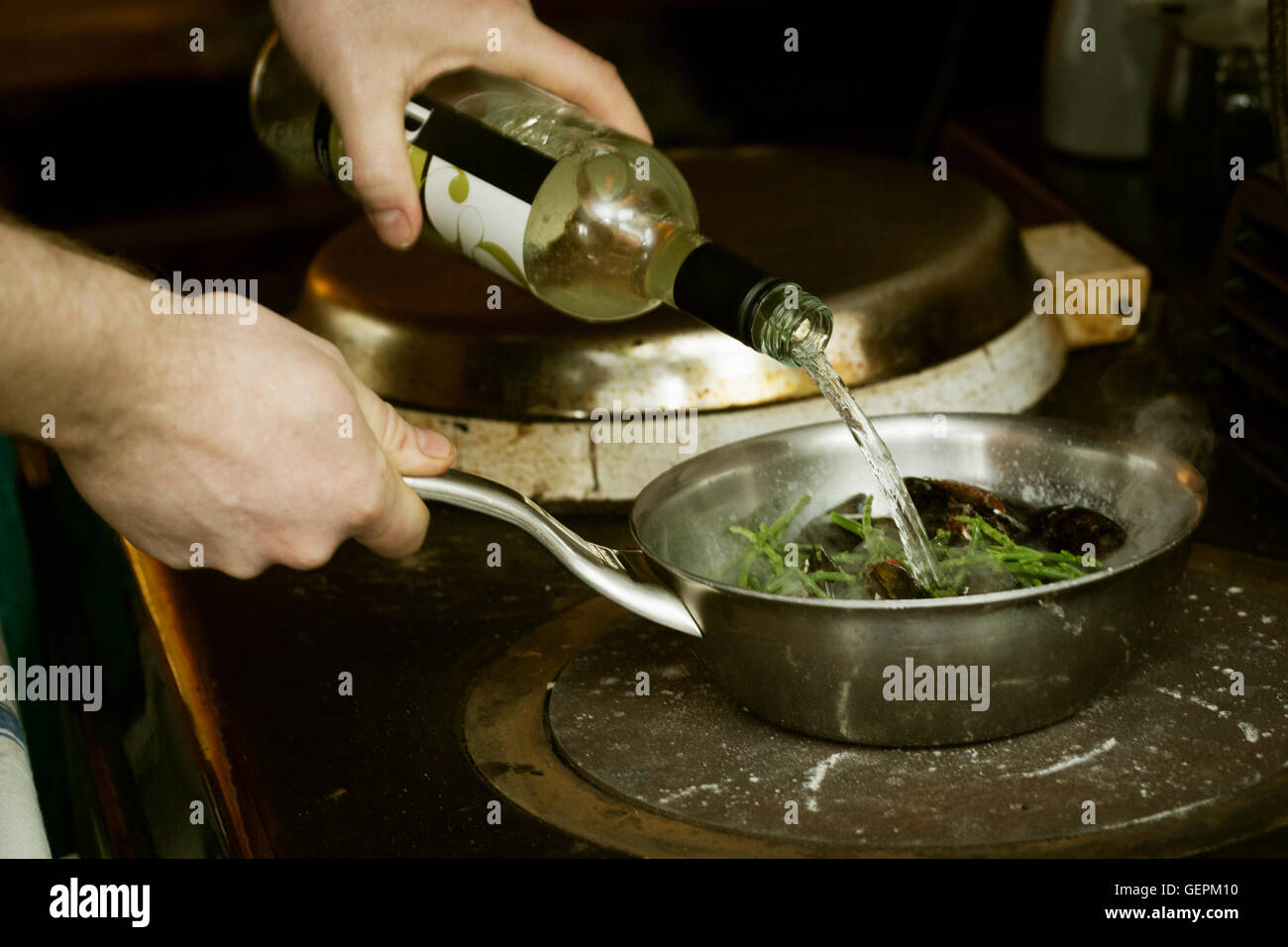 Chef adding white wine to a pan of Black Mussels and samphire. Stock Photo