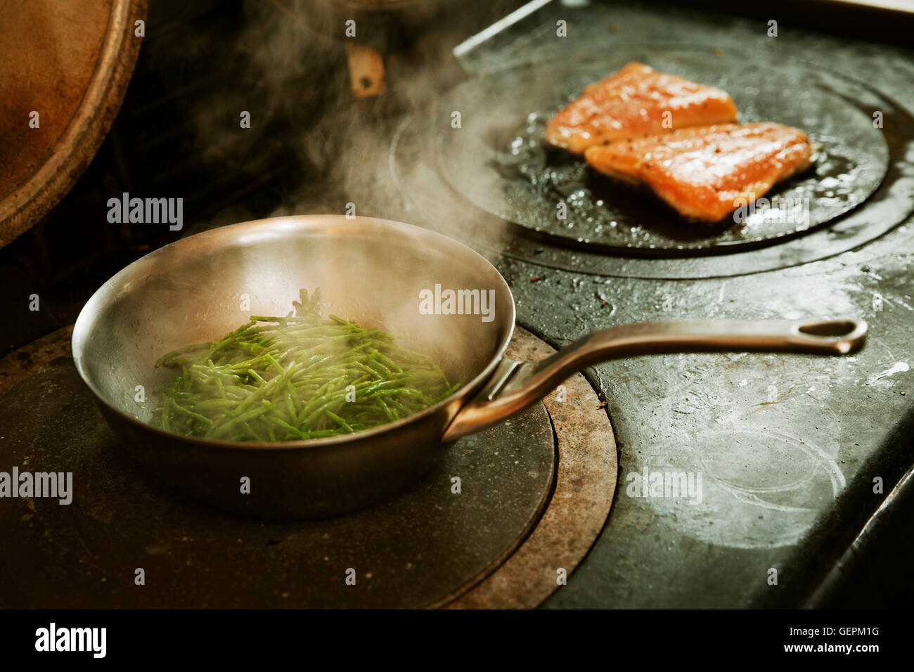 Frying pan with samphire and a fish fillet grilled on a stove. Stock Photo