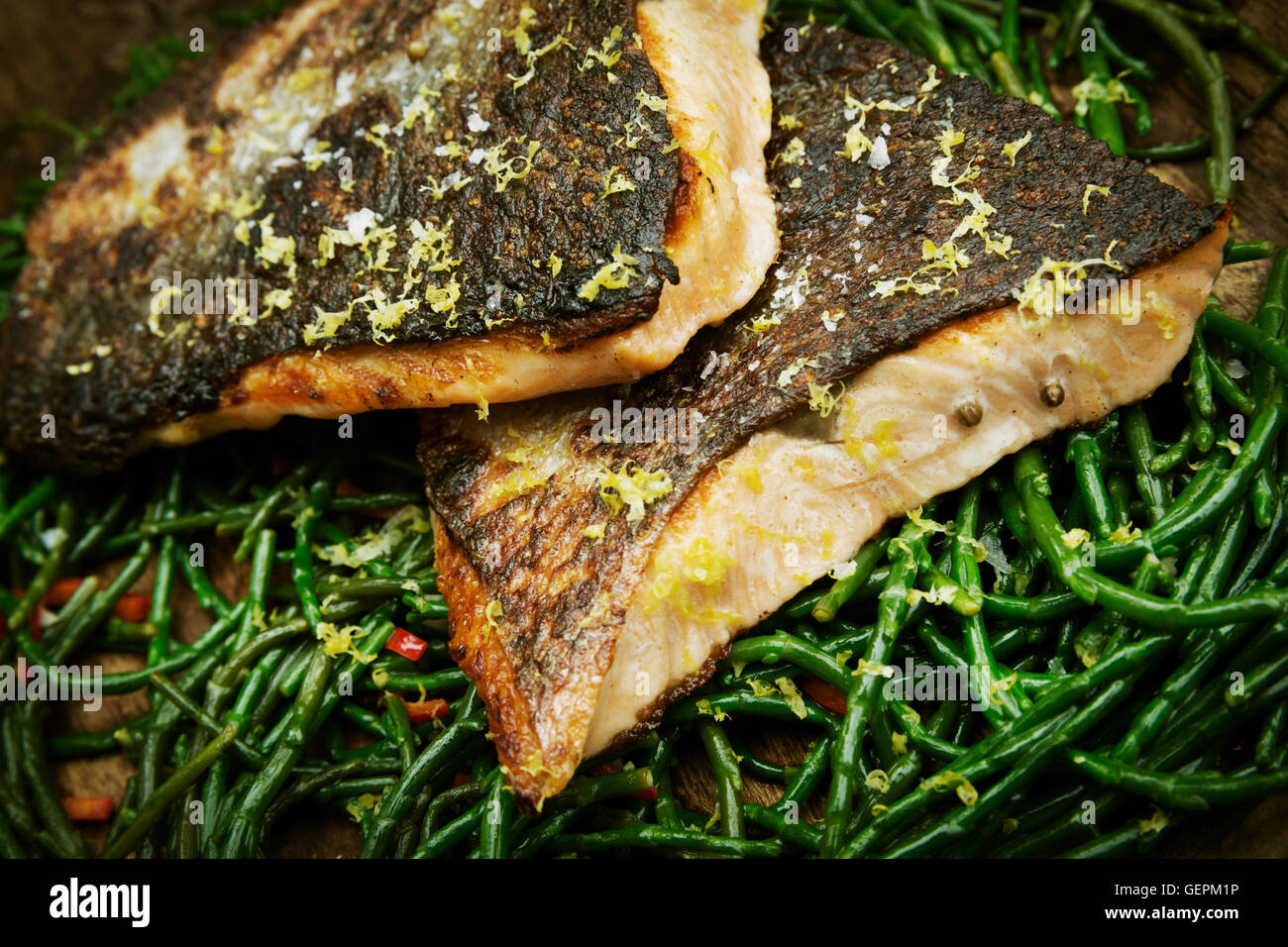 Close up of grilled fish fillets with crispy skin on a bed of samphire. Stock Photo