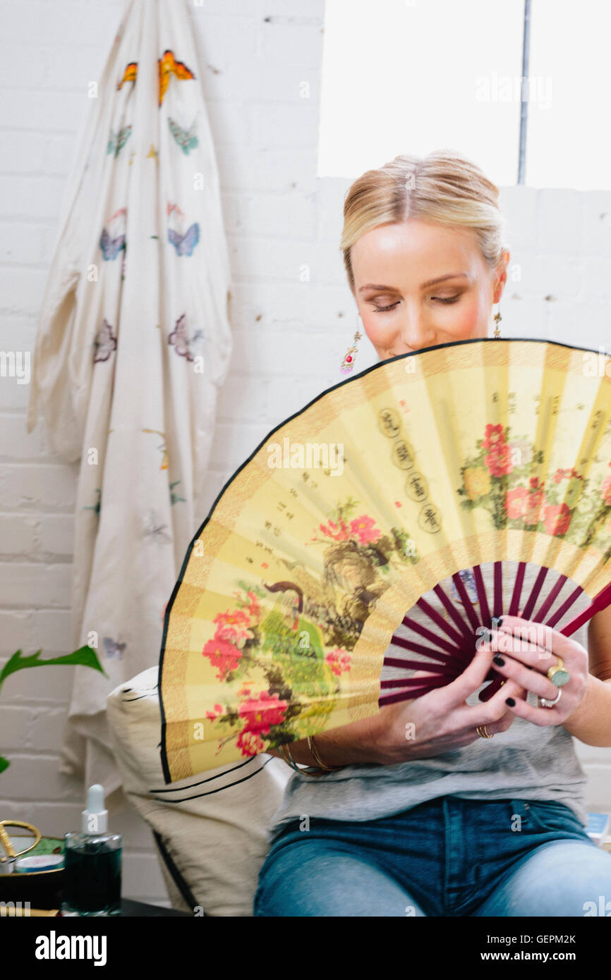 A woman holding an open Oriental fan hiding her face. Stock Photo