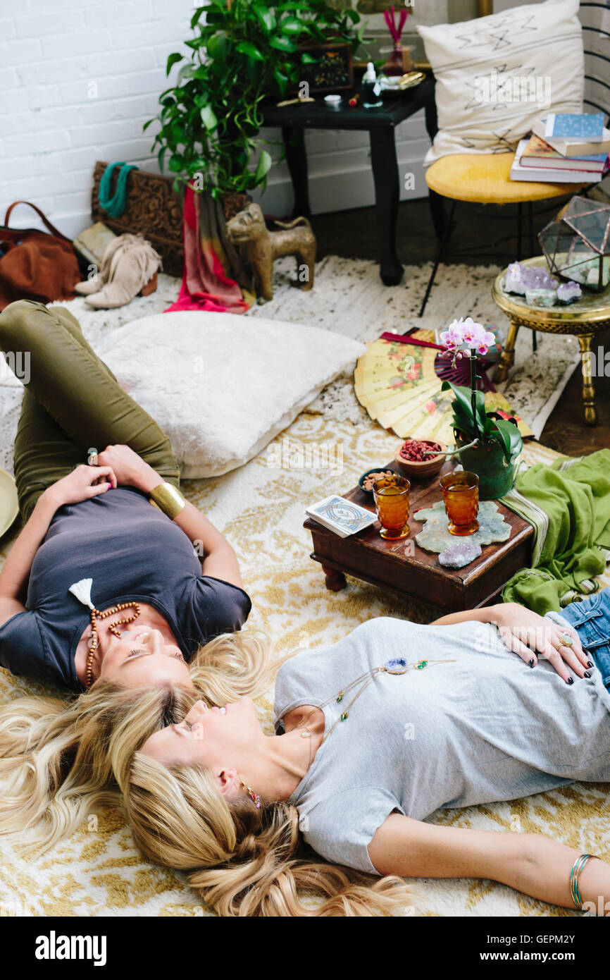 Two women lying on the floor of a room strewn with cushions and personal possessions. Stock Photo