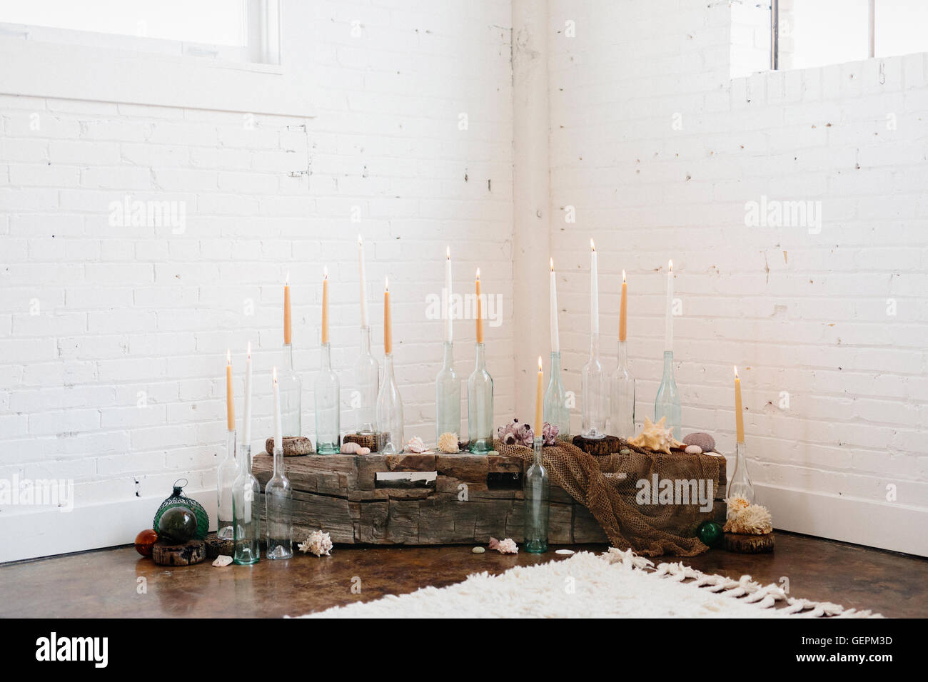 A group of tall lit candles in clear glass bottles arranged in a corner. Stock Photo