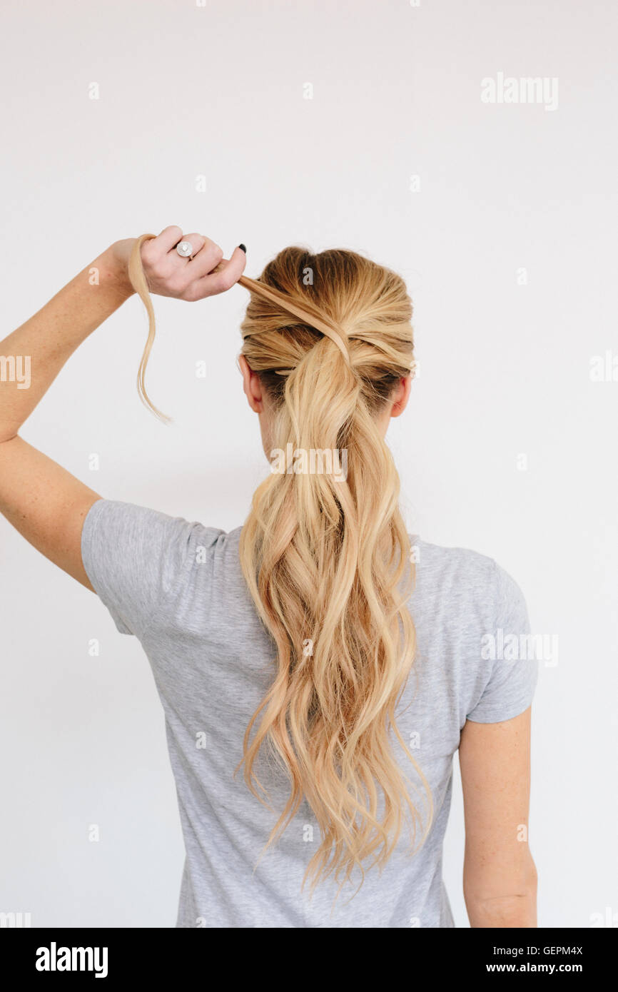 A Young Woman With Long Blond Wavy Hair Tying A Ponytail Back