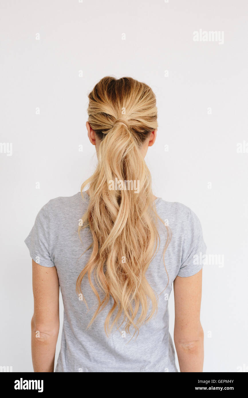 A young woman with long blond wavy hair tied in a ponytail. Back view. Stock Photo