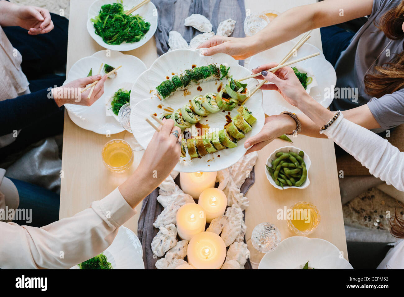 Overhead view of four people sharing a meal, plates of sushi and a table setting for a celebration meal. Stock Photo