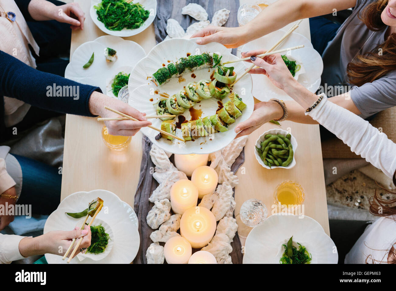 Overhead view of four people sharing a meal, plates of sushi and a table setting for a celebration meal. Stock Photo