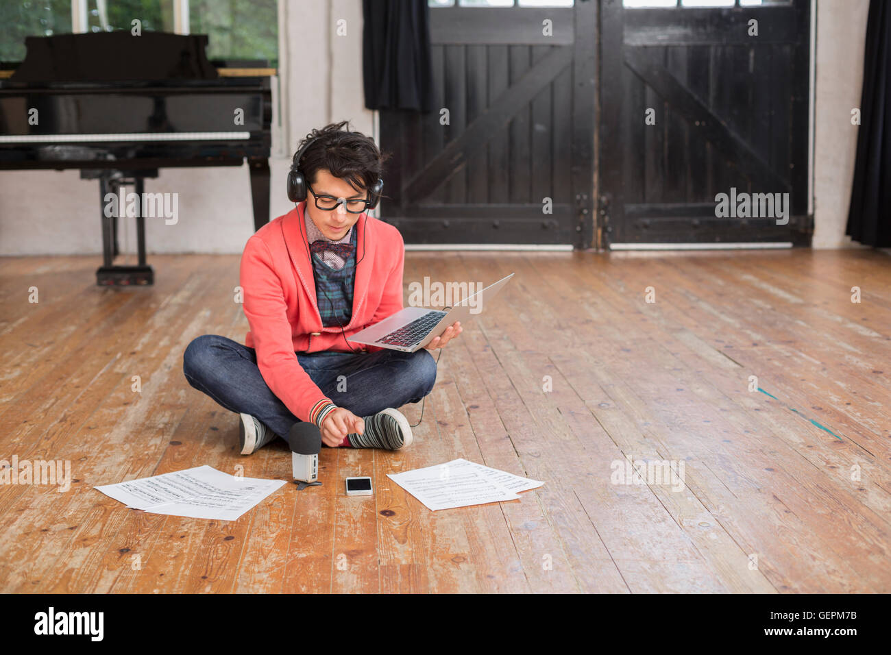 Young man sitting on the floor in a rehearsal studio, using a laptop computer, looking at sheet music. Stock Photo