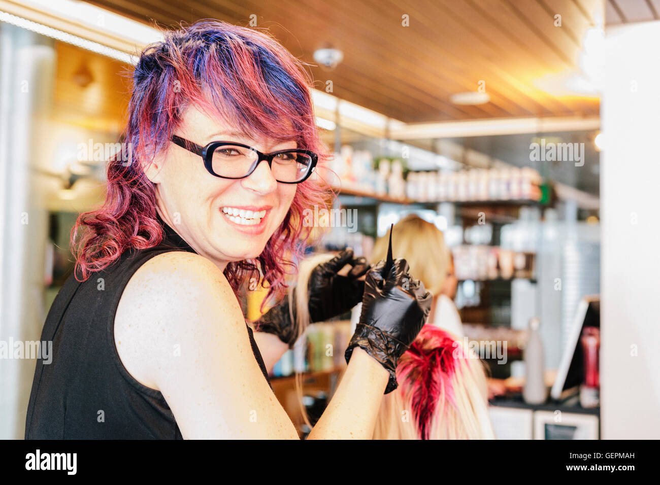 A hair colourist in gloves applying red hair dye to a client's blonde hair with a brush. Stock Photo