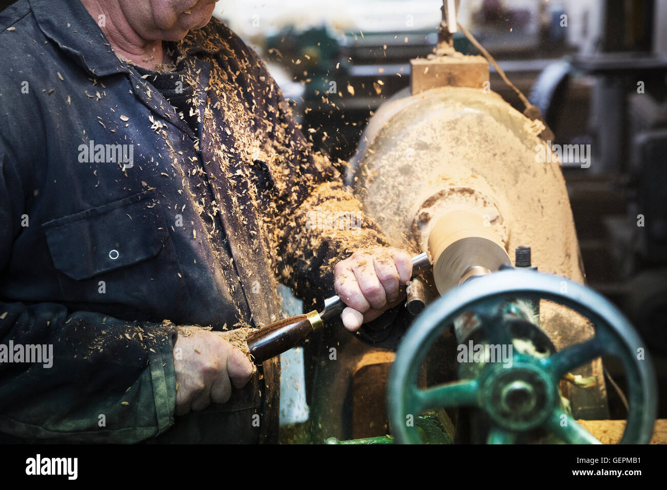 Man standing at a woodworking machine in a carpentry workshop, turning a piece of wood. Stock Photo