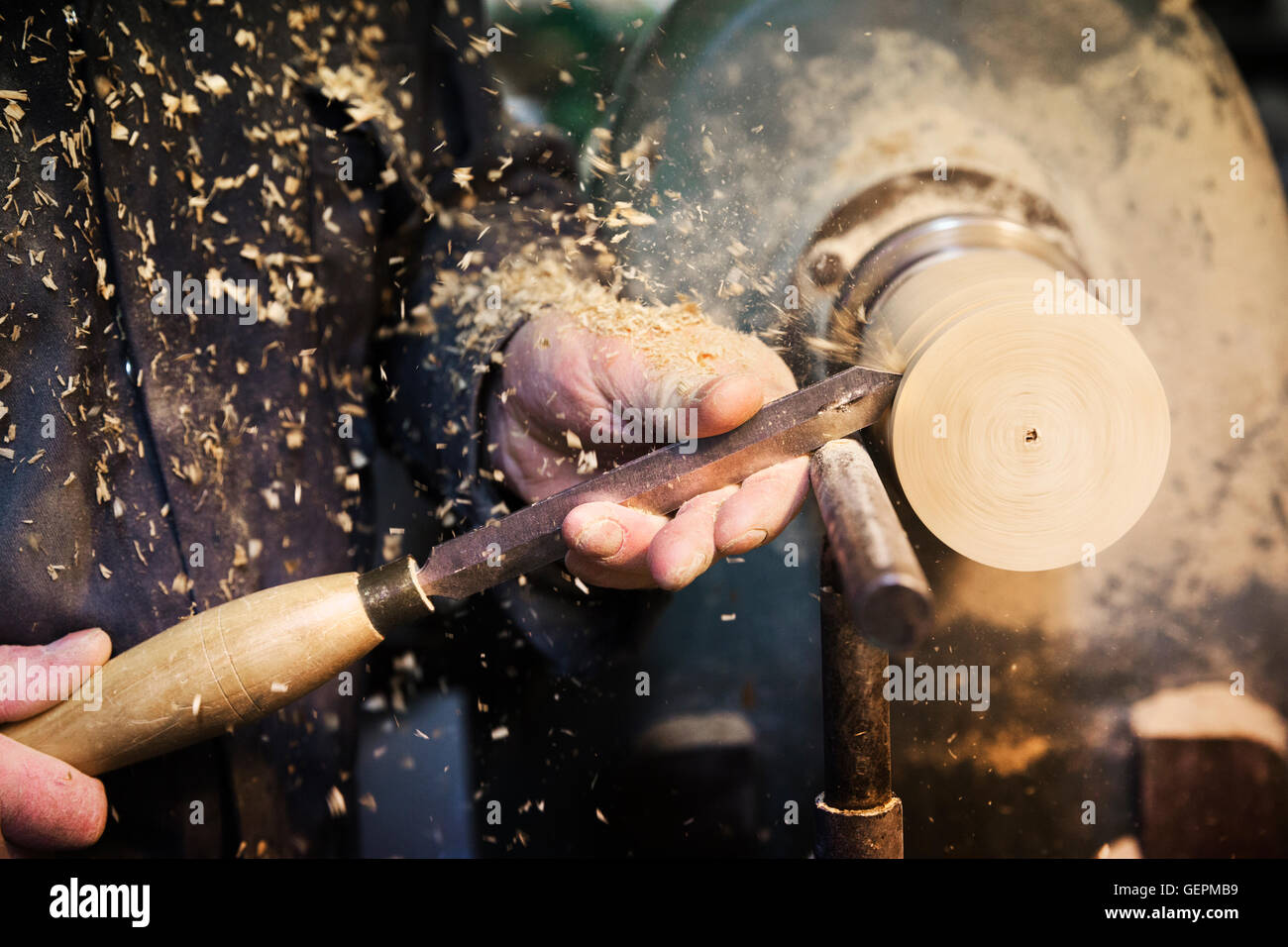man standing at a woodworking machine in a carpentry workshop, turning a piece of wood. Stock Photo