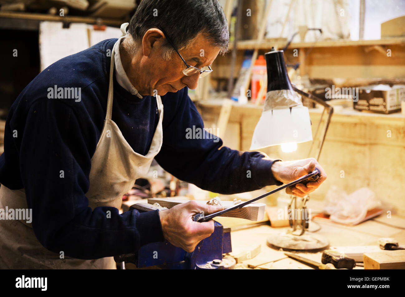 Man standing at a work bench in a carpentry workshop, working on a piece of wood secured in a bench vice. Stock Photo