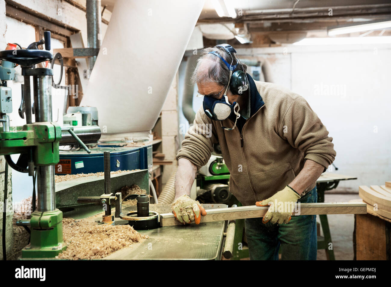 Man standing in a carpentry workshop, wearing a respirator and hearing protector, working on a piece of wood. Stock Photo