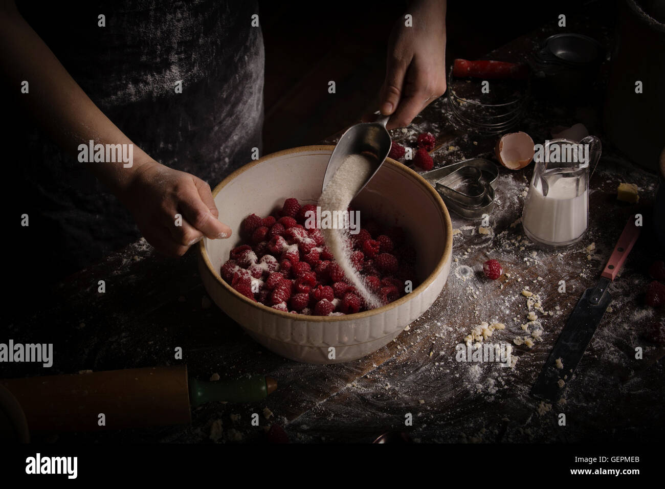 Valentine's Day baking, woman preparing fresh raspberries in a bowl, adding sugar. Stock Photo