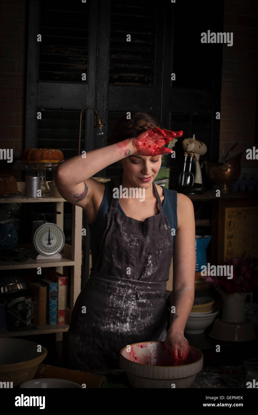 Valentine's Day baking, young woman standing in a kitchen, preparing raspberry jam, wiping her hand on her forehead. Stock Photo