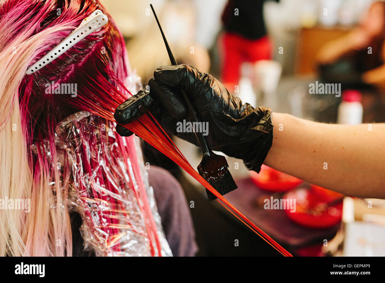 A hair colourist applying pink hair colour to a client's long blonde hair. Stock Photo