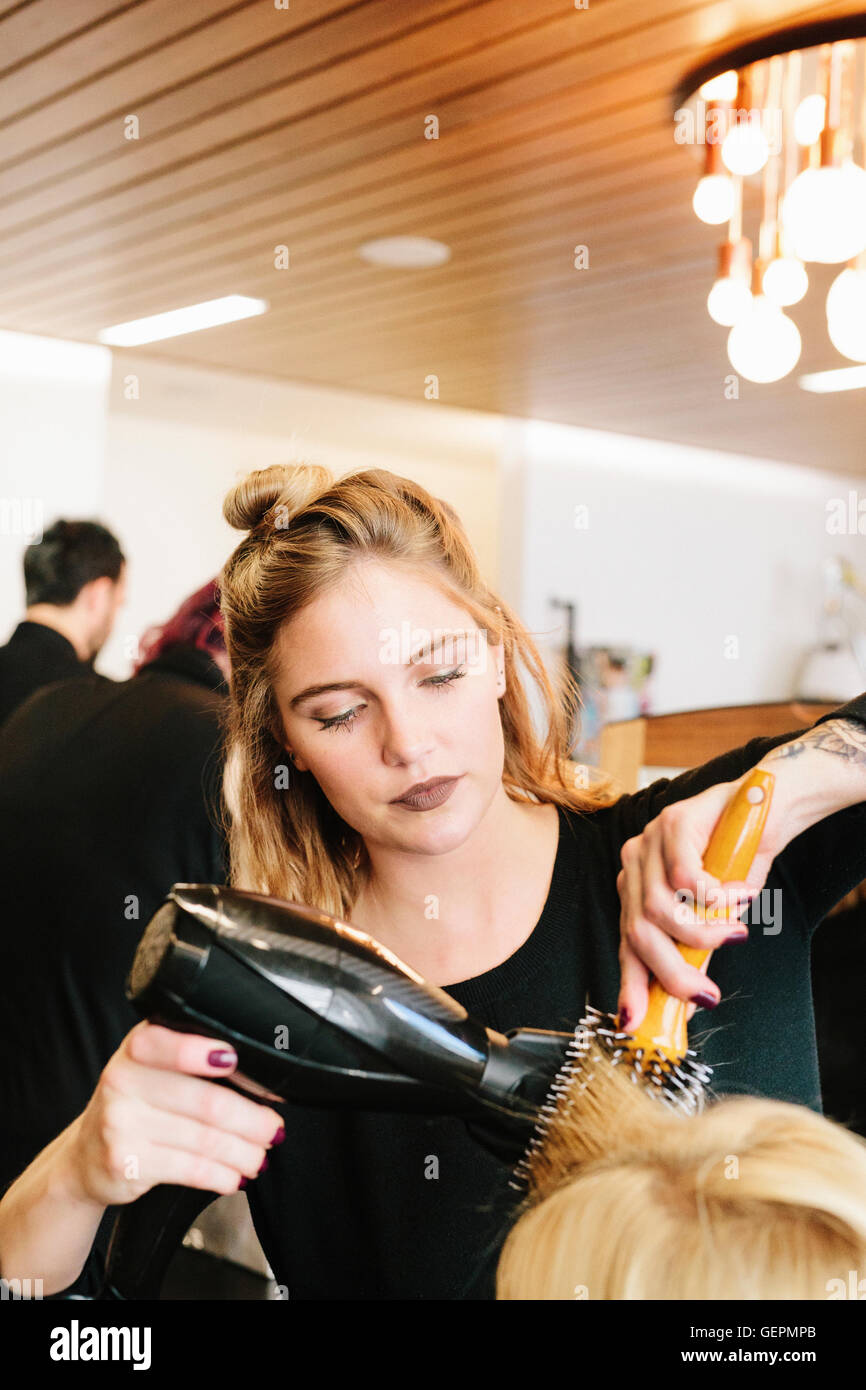 A hair stylist blowdrying a client's blonde hair. Stock Photo