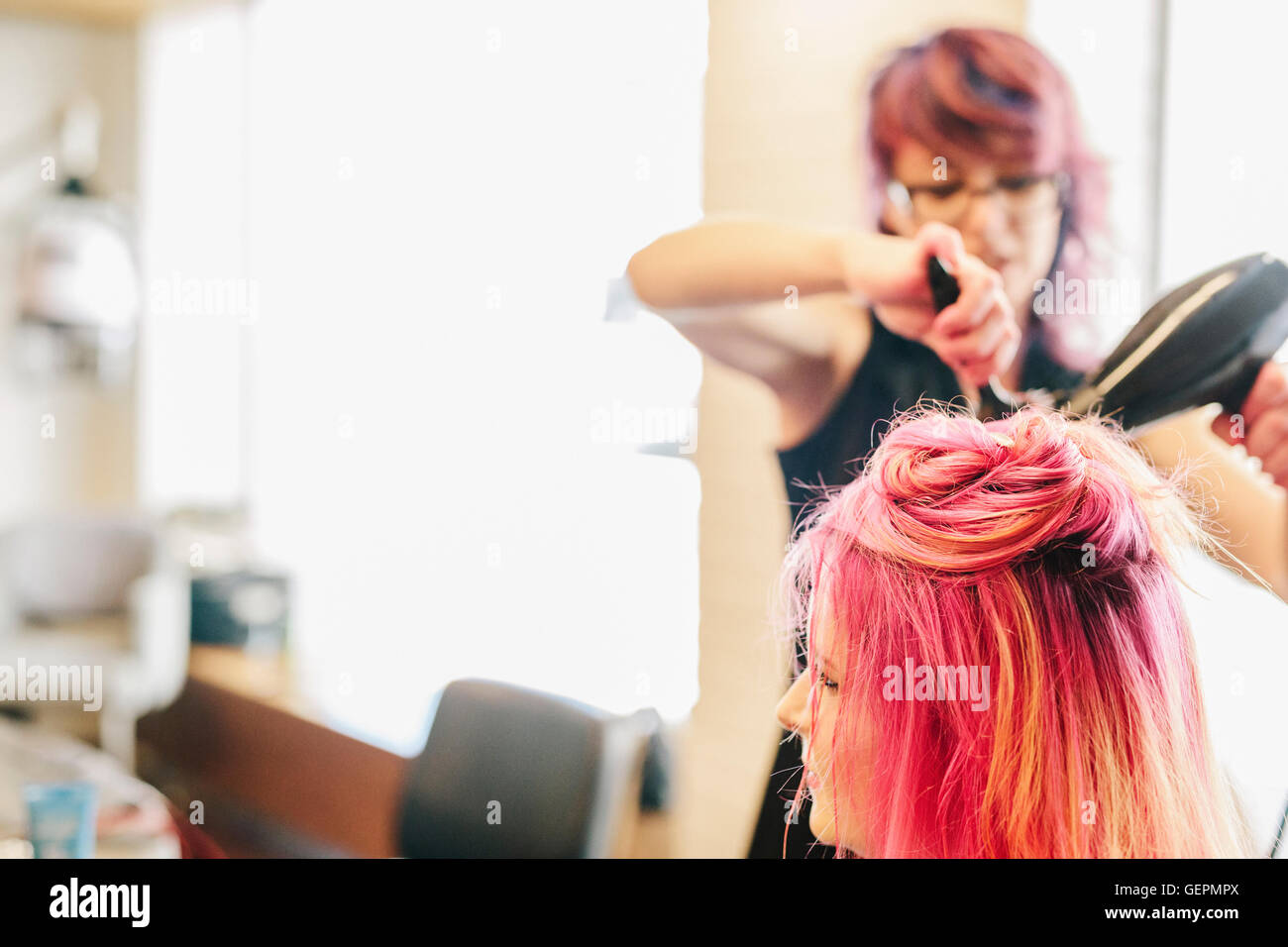 A hair stylist blow-drying a client's long pink dyed hair. Stock Photo