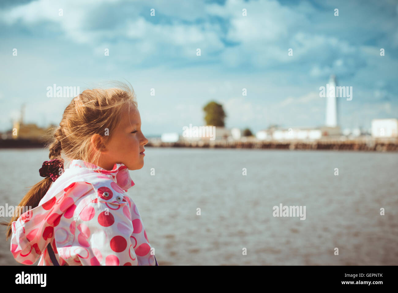 Girl in a bright pink jacket on background of view from the promenade to the pier with a lighthouse and ships in Kronstadt Stock Photo