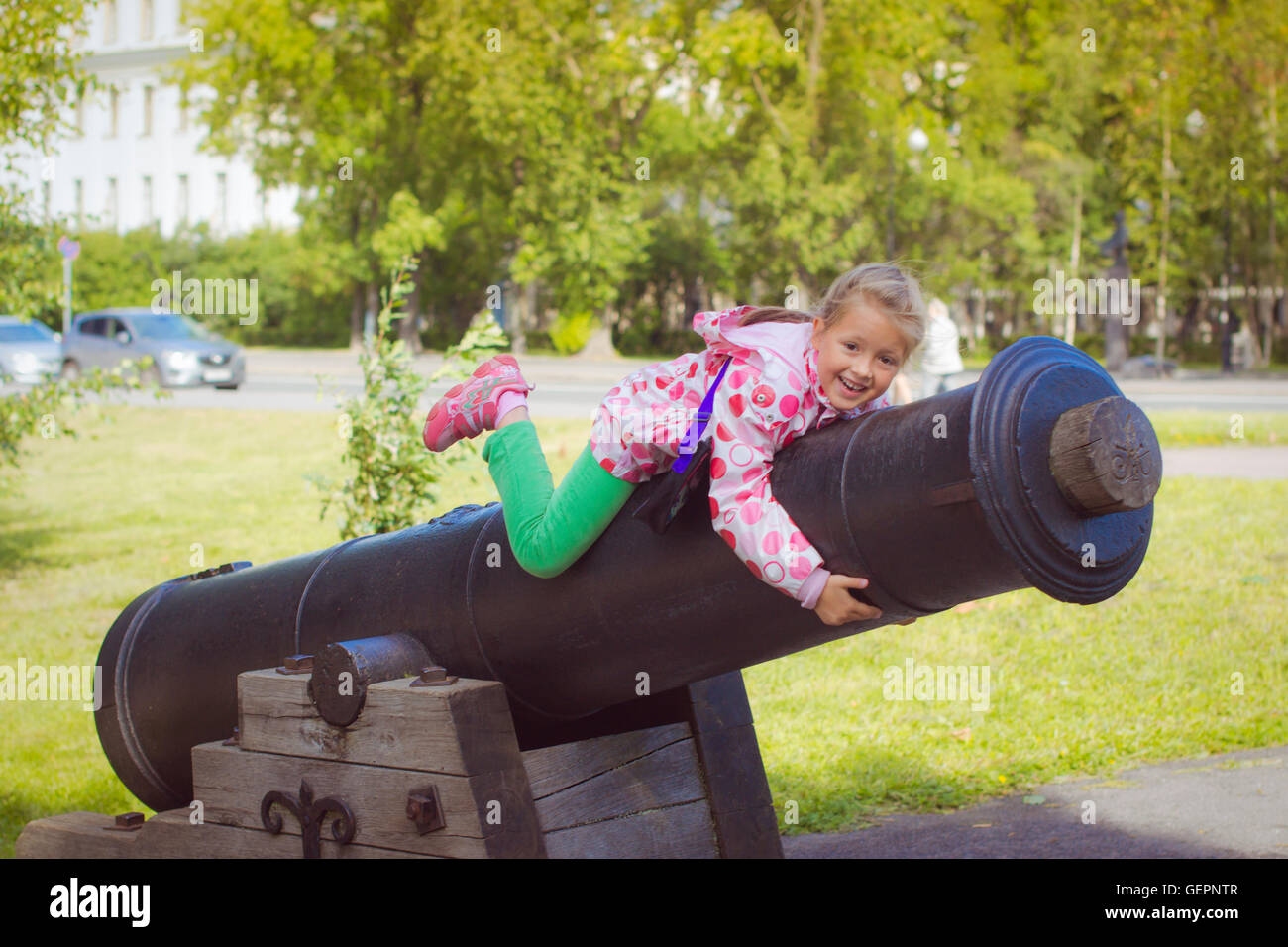 Girl in a bright pink jacket, sitting on an old cannon on the ship's promenade in Kronstadt, Russia Stock Photo