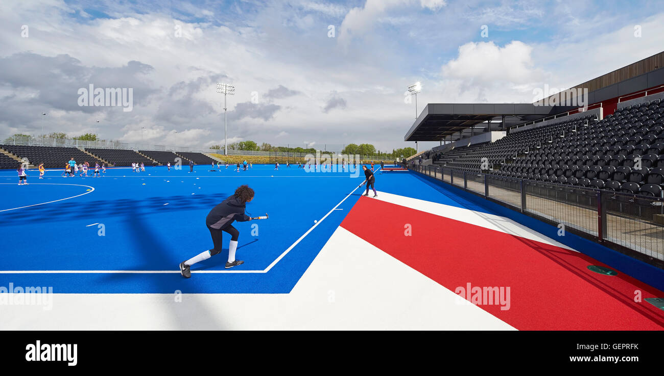 Activity on hockey field in blue with spectator stand. Eton Manor - Lee Valley Hockey and Tennis Centre, London, United Kingdom. Architect: Stanton Williams, 2014. Stock Photo