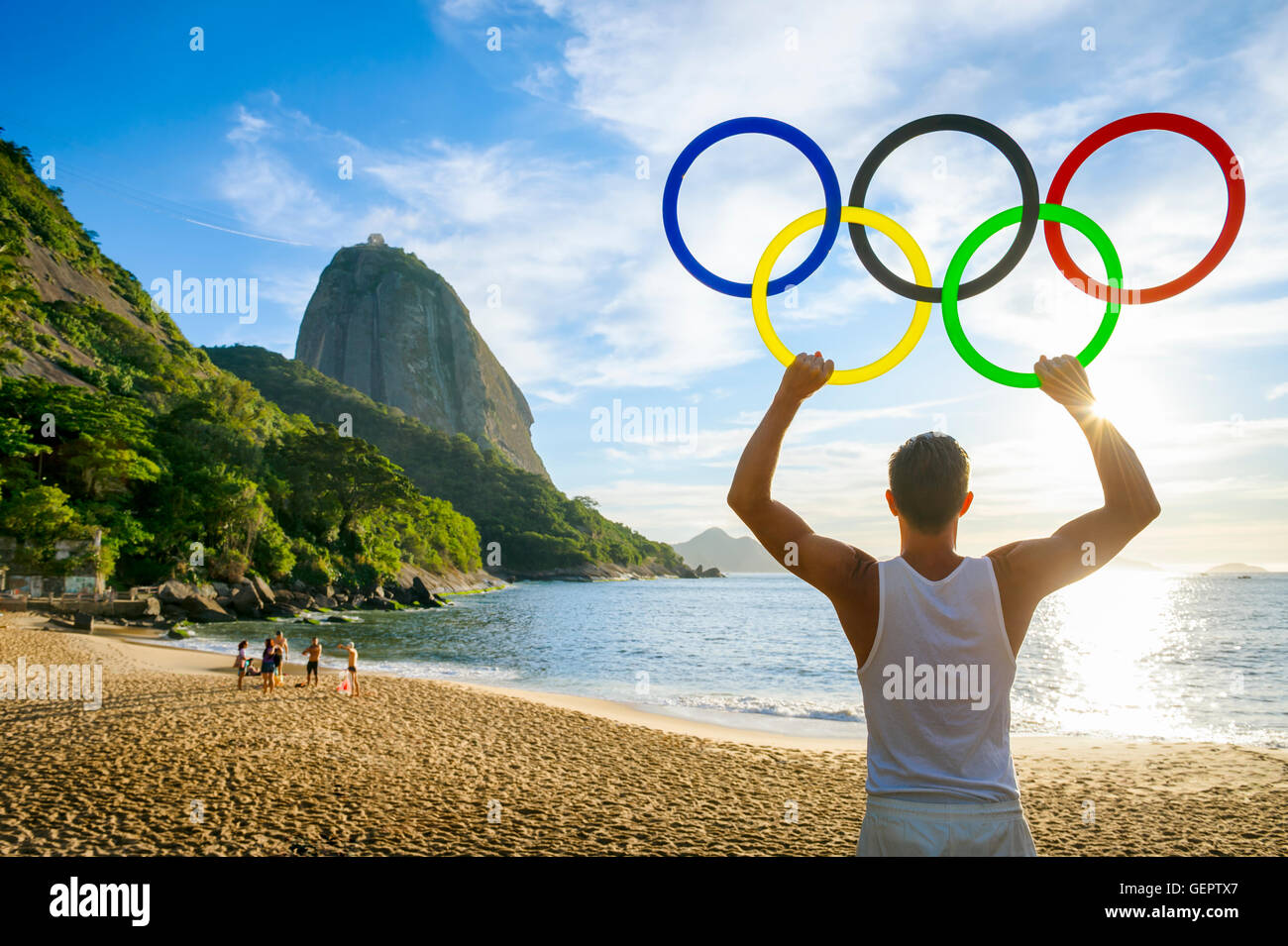 RIO DE JANEIRO - OCTOBER 31, 2015: Athlete holds Olympic rings in front of a sunrise silhouette of Sugarloaf Mountain. Stock Photo