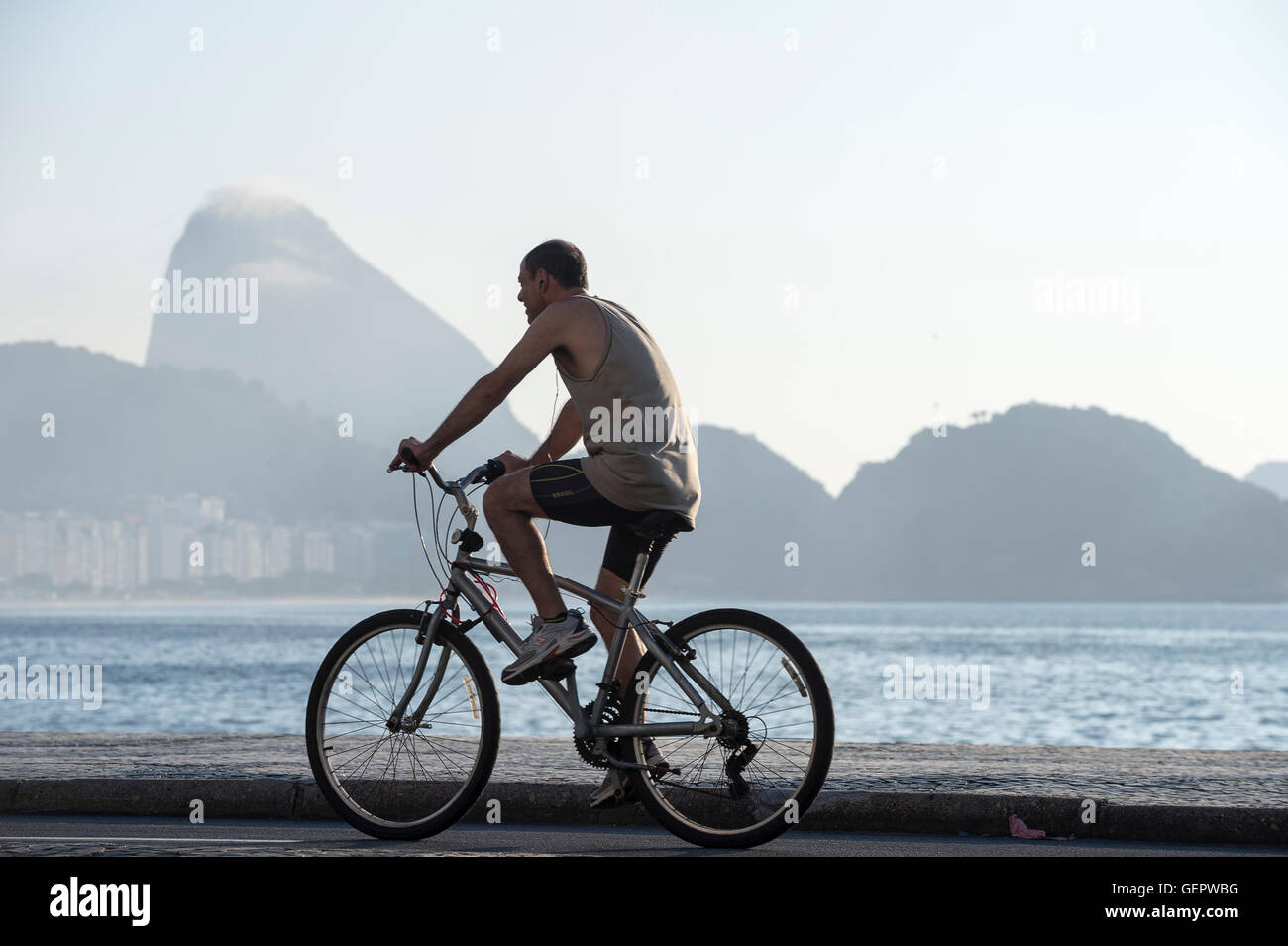 RIO DE JANEIRO - APRIL 3, 2016: Young Brazilian man rides a bicycle on the beachfront boardwalk at Copacabana Beach. Stock Photo