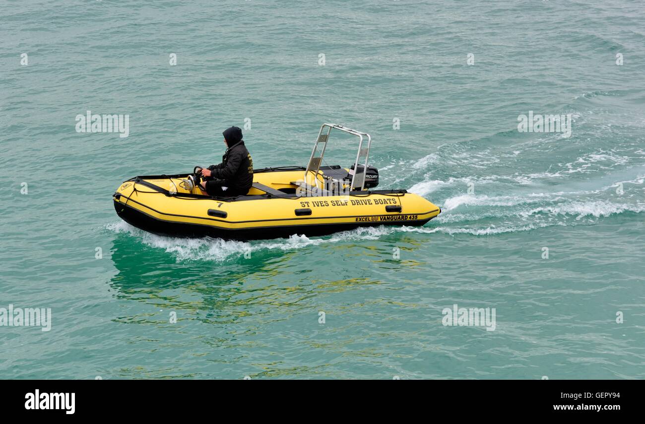 A man wearing hoody driving a St Ives self drive hire boat Cornwall England UK Stock Photo
