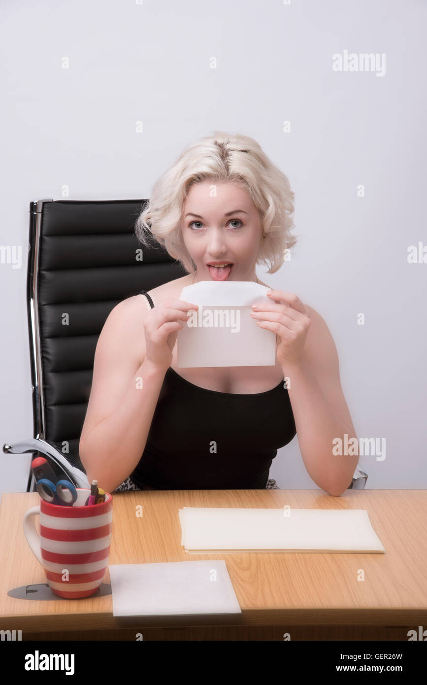 SECRETARY WORKING AT A DESK.  Secretary licking an envelope Stock Photo