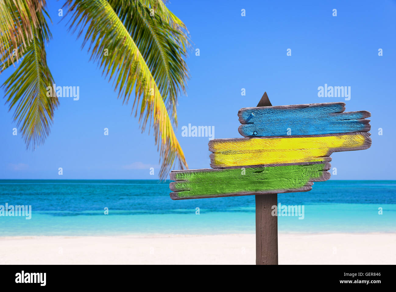 Pastel colored wooden direction signs, beach and palm tree background Stock Photo