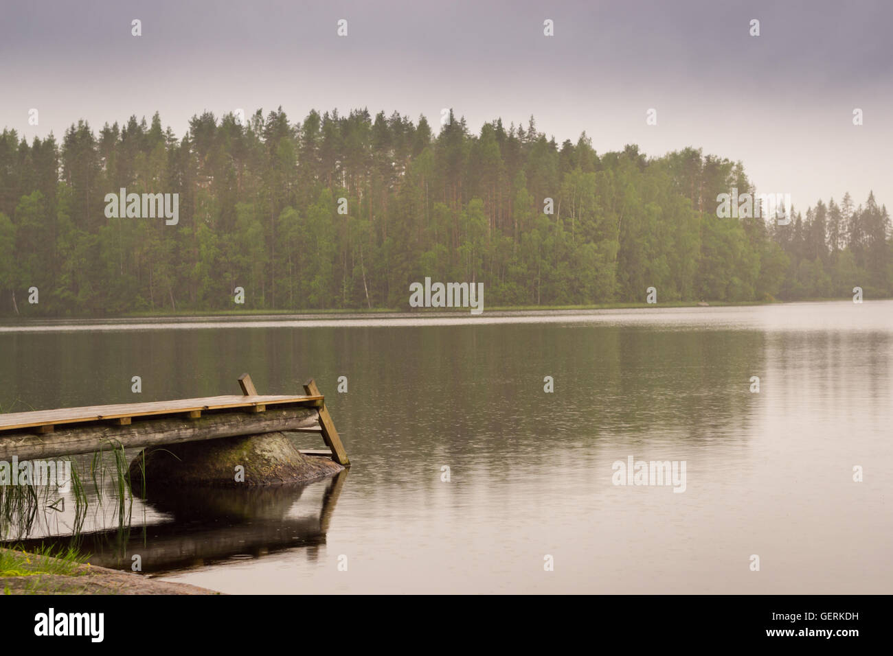 Cloudy summer day on the lake. Wooden boat pier overlooking the water and island. Area for summer camping in the woods. Finland Stock Photo