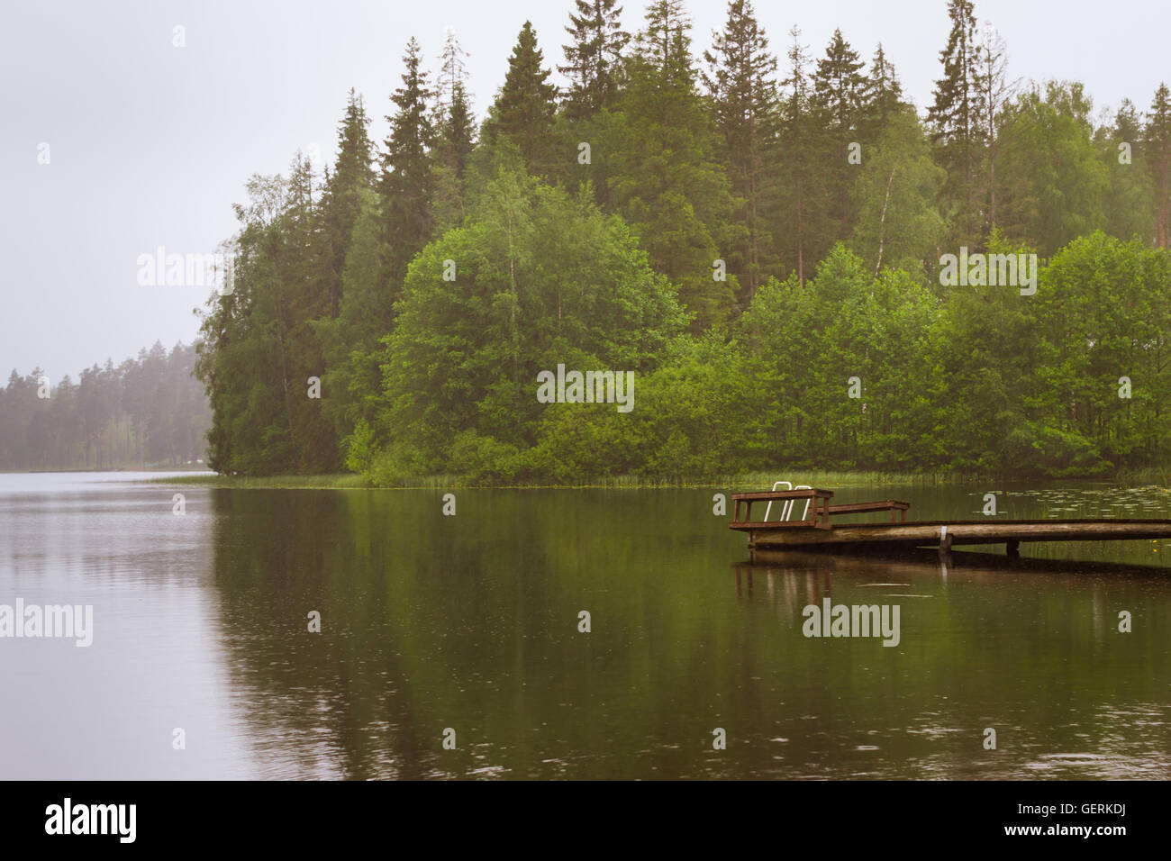 Cloudy summer day on the lake. Wooden boat pier overlooking the water and island. Area for summer camping in the woods. Finland Stock Photo
