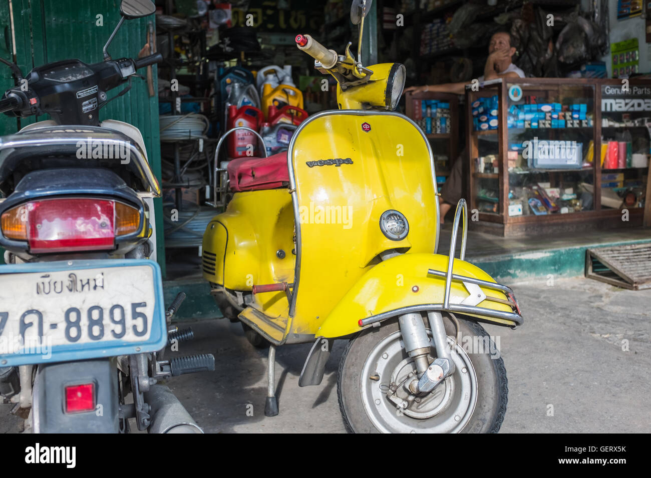 Yellow Vespa parked outside parts shop,Chiang Mai Thailand Stock Photo